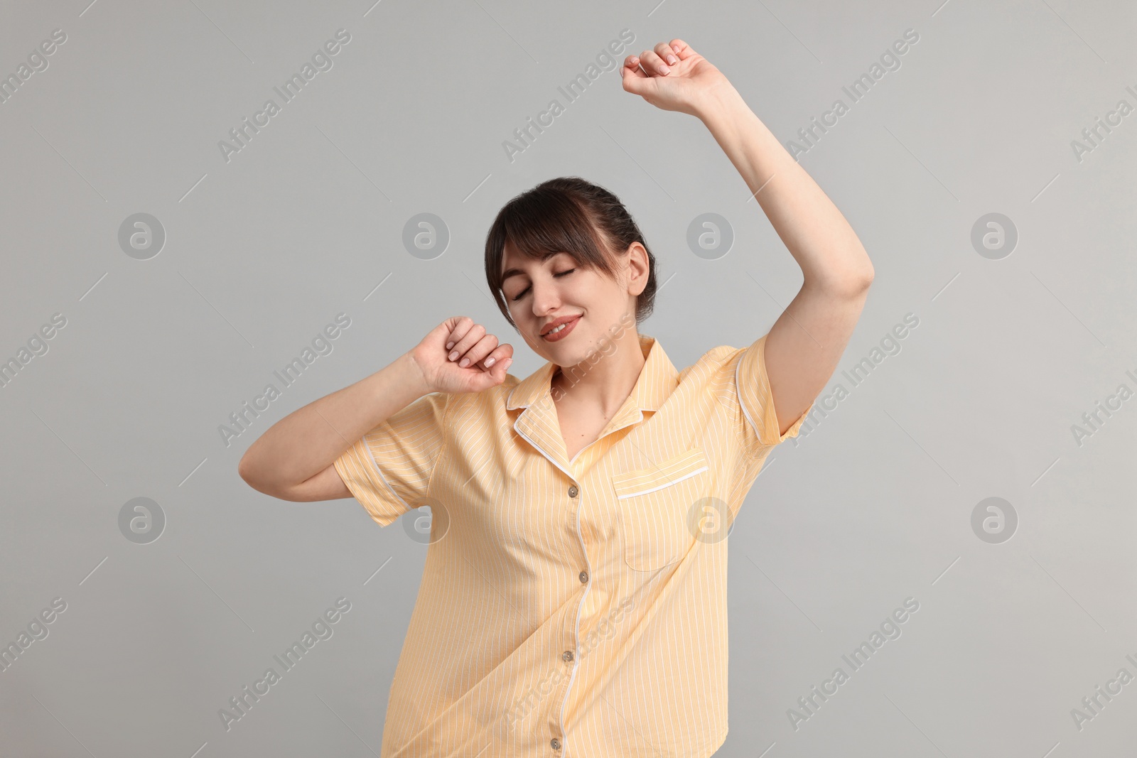 Photo of Woman in pyjama stretching on grey background