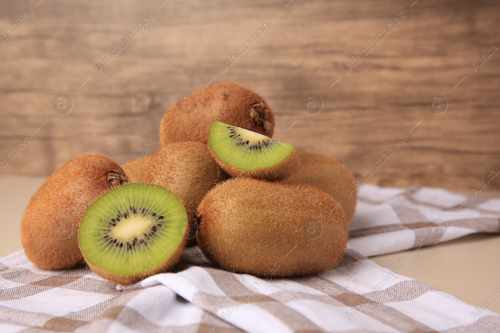 Photo of Heap of whole and cut fresh kiwis on beige table, space for text