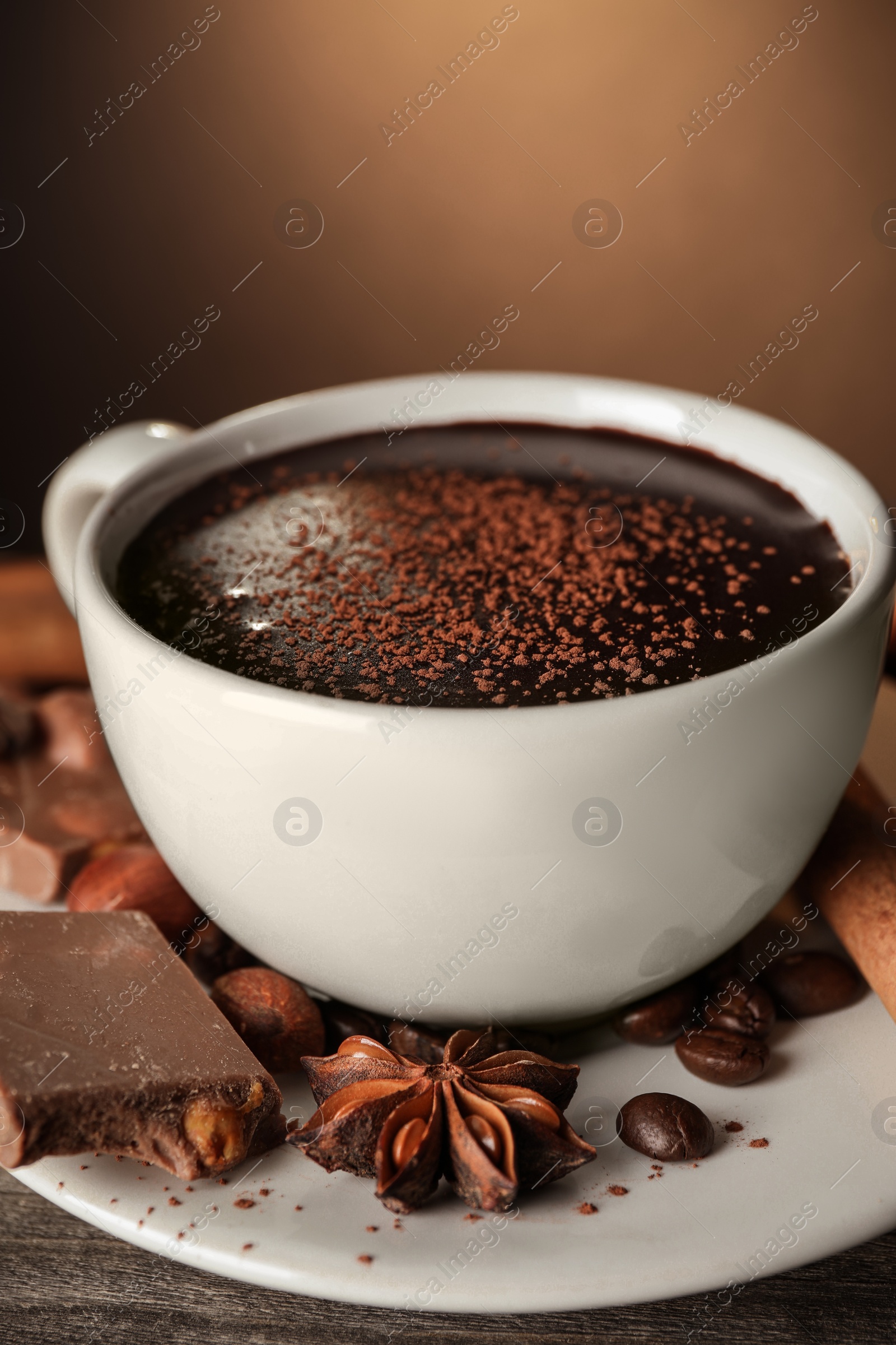 Photo of Cup of delicious hot chocolate, spices and coffee beans on wooden table