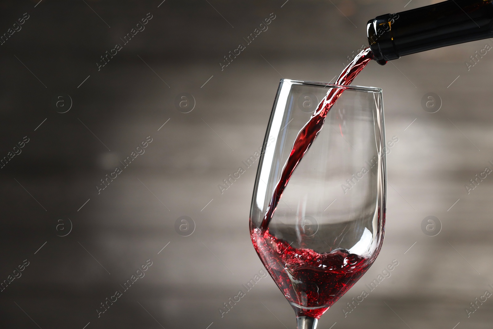 Photo of Pouring red wine into glass against gray background, closeup. Space for text