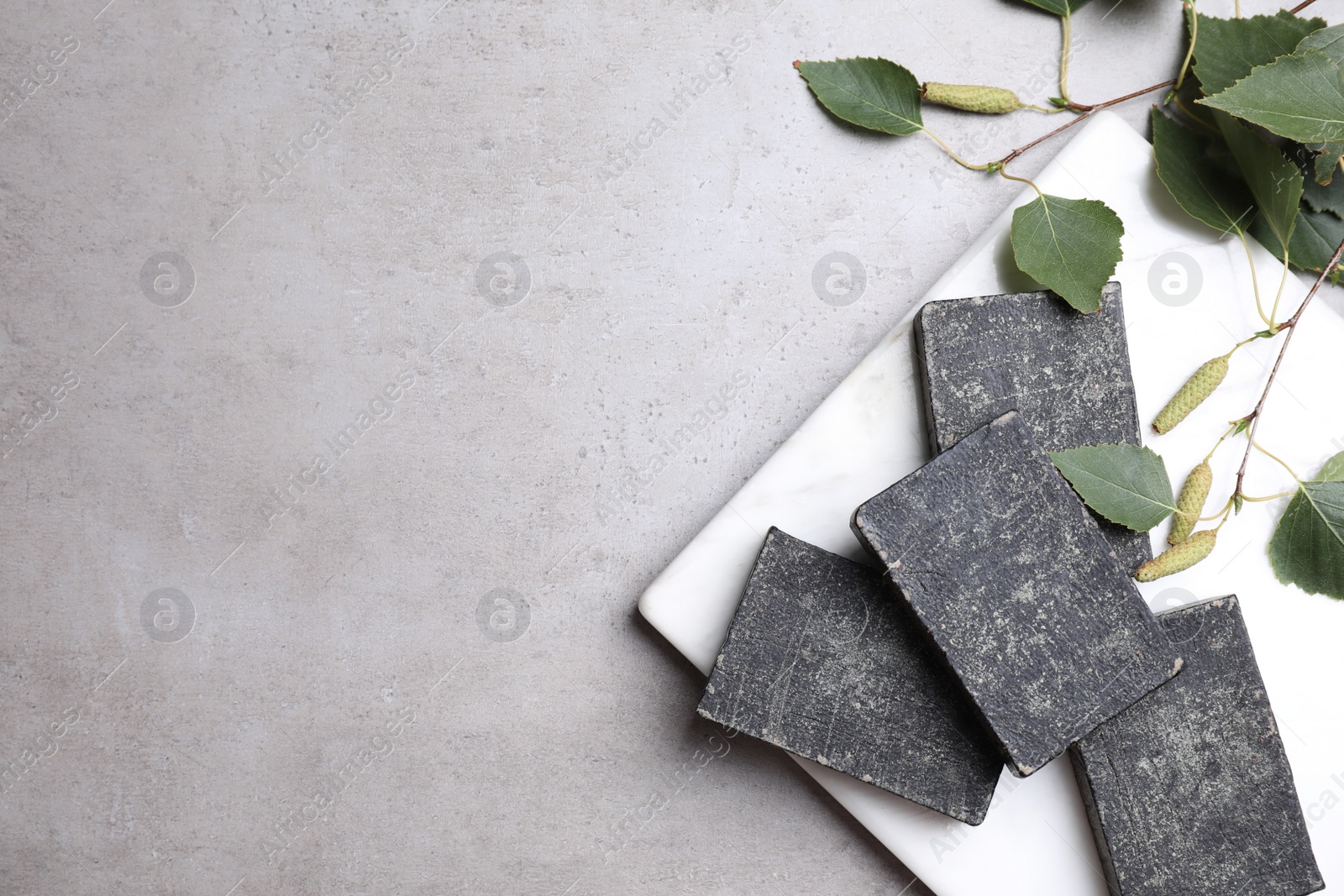 Photo of Natural tar soap bars and birch branches on light grey stone table, flat lay. Space for text