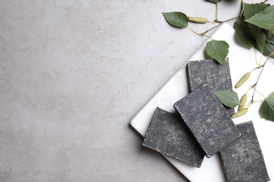 Natural tar soap bars and birch branches on light grey stone table, flat lay. Space for text