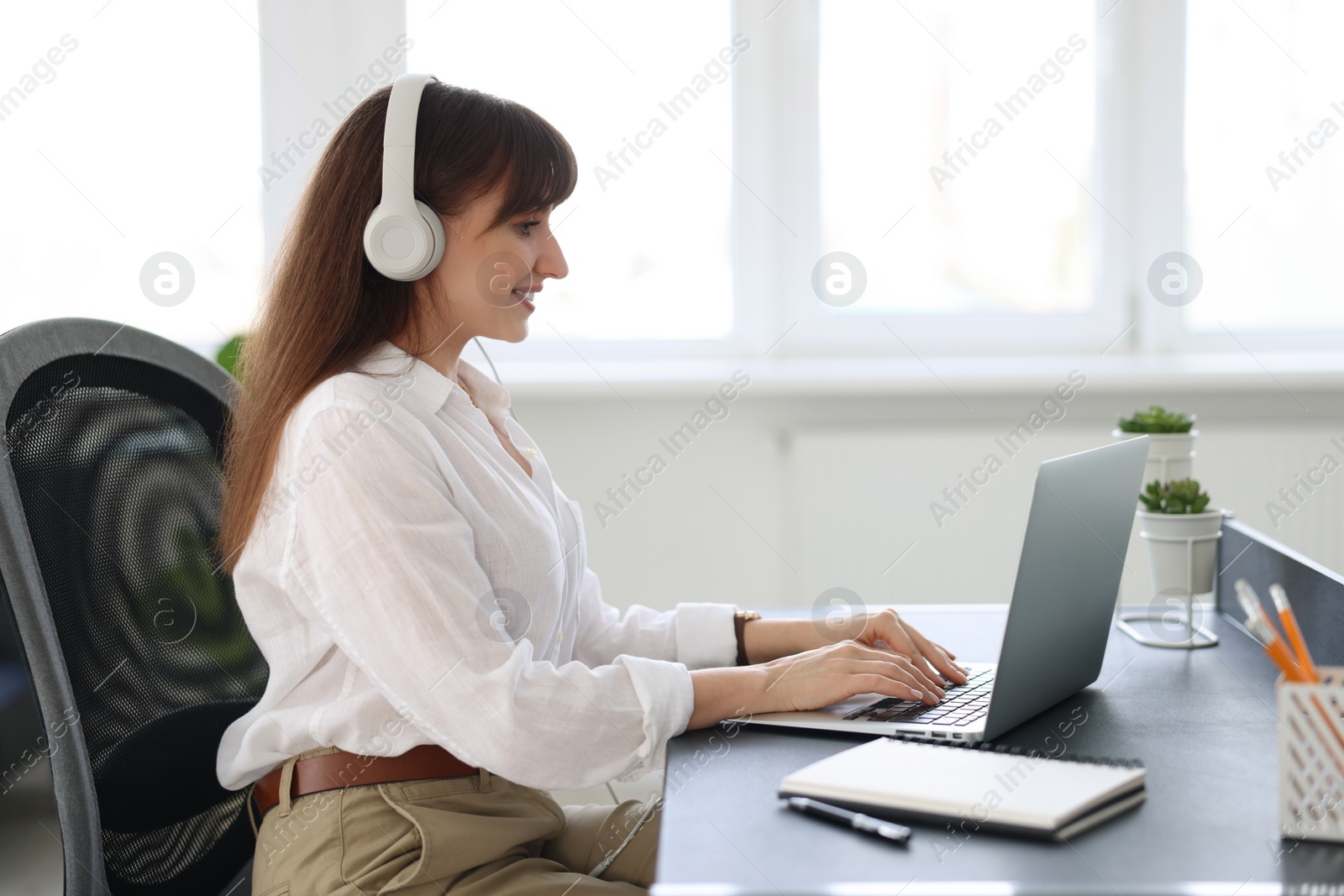 Photo of Woman in headphones watching webinar at table in office