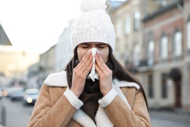 Photo of Woman with tissue blowing runny nose outdoors. Cold symptom