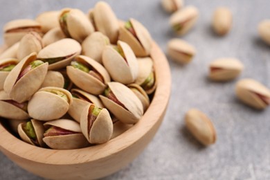 Photo of Delicious pistachios in bowl on grey textured table, closeup