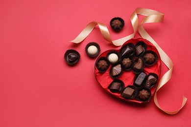 Heart shaped box with delicious chocolate candies and ribbon on red background, flat lay. Space for text