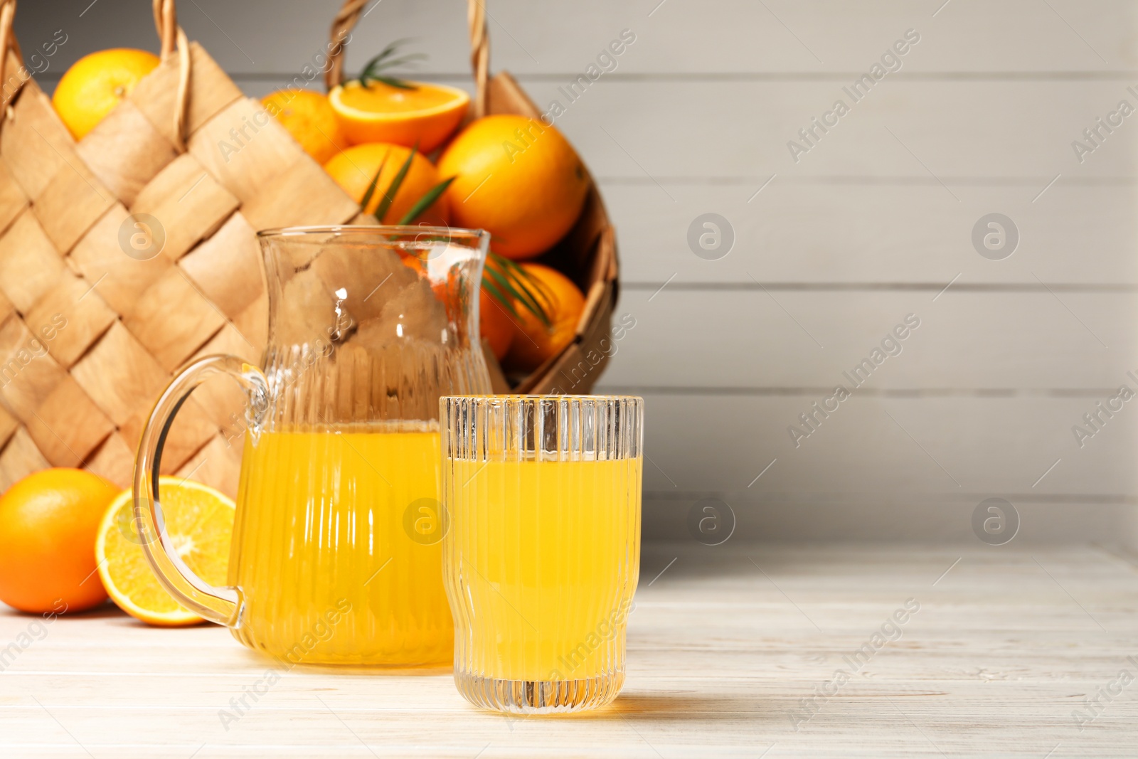 Photo of Tasty freshly made orange juice on white wooden table. Space for text