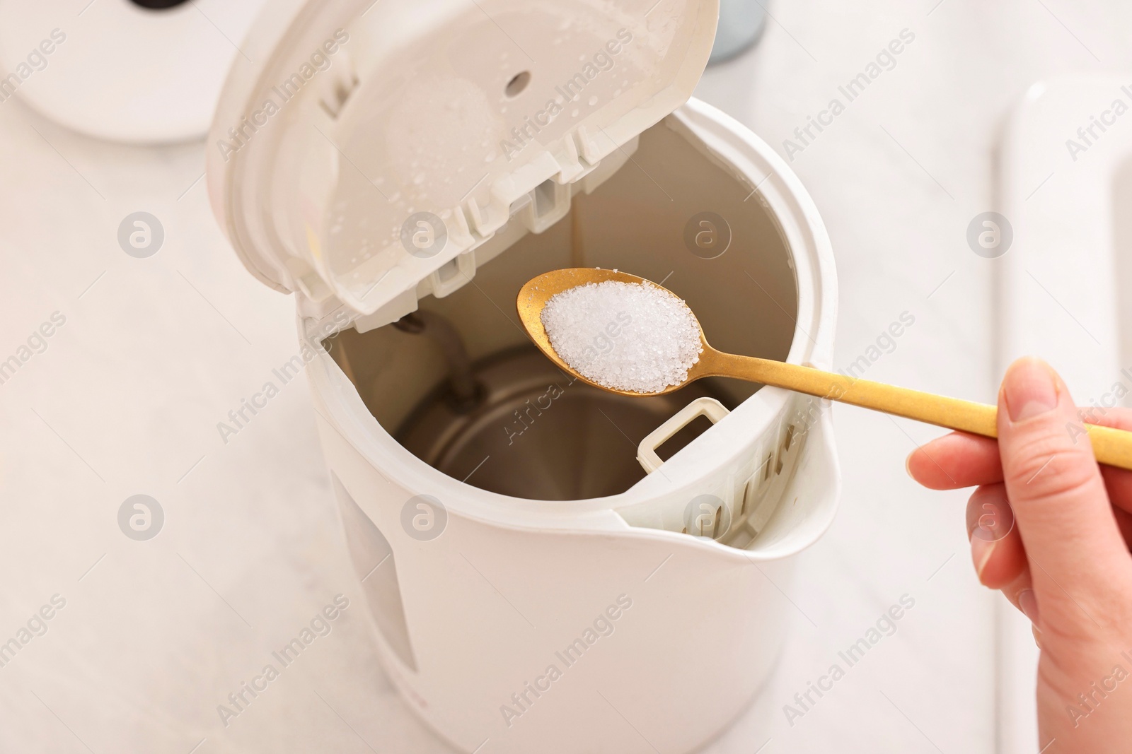 Photo of Cleaning electric kettle. Woman adding baking soda to appliance at table, above view