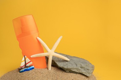 Photo of Sand with bottle of sunscreen, starfish, stone and ship figure against orange background, space for text. Sun protection