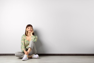 Photo of Beautiful young girl sitting on floor near white wall. Space for text