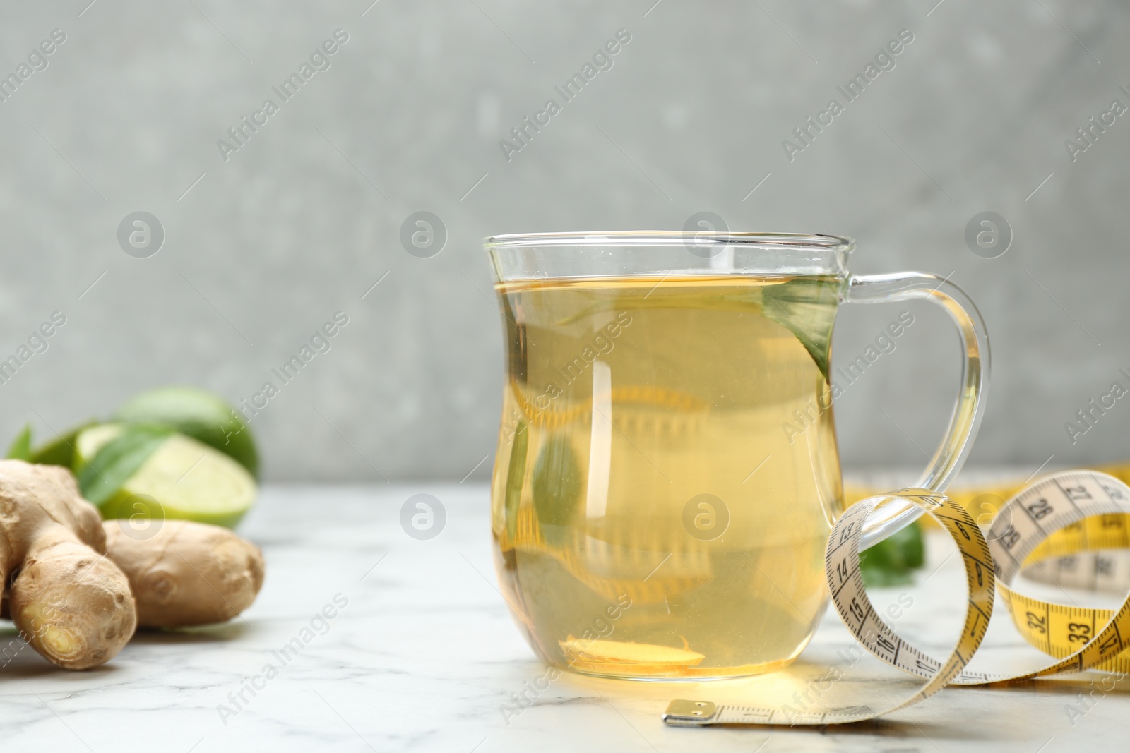 Photo of Diet herbal tea, measuring tape and ginger on white marble table