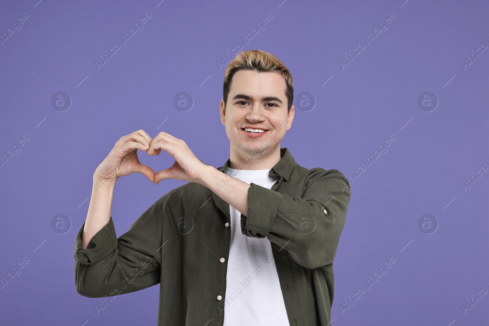 Photo of Young man showing heart gesture with hands on purple background