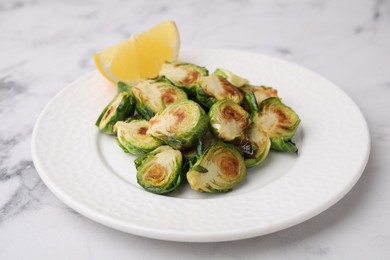 Delicious roasted Brussels sprouts and slice of lemon on white marble table, closeup