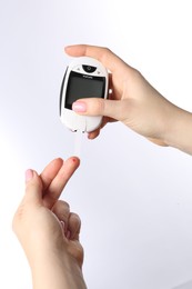 Diabetes. Woman checking blood sugar level with glucometer on white background, closeup