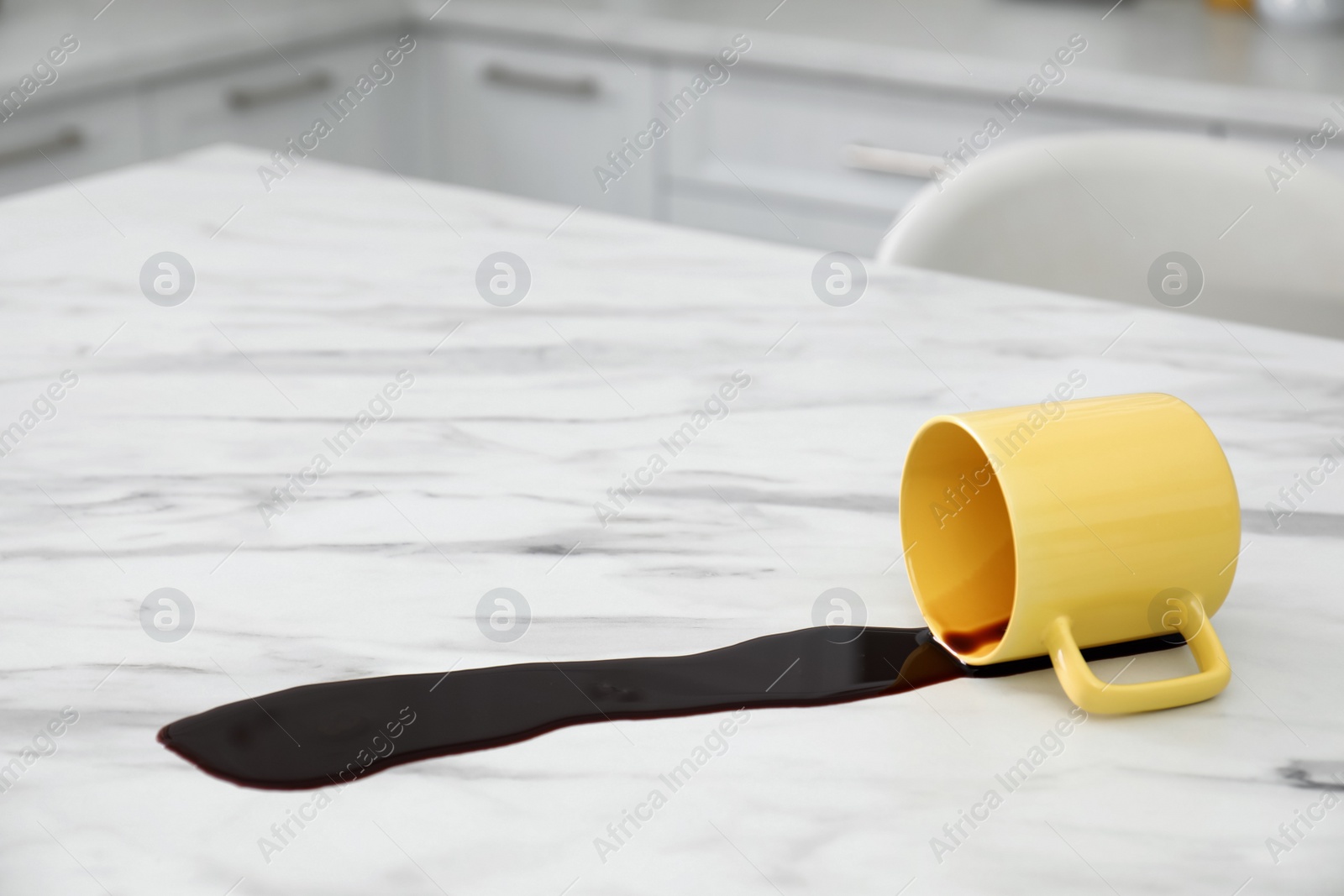 Photo of Overturned cup and spilled coffee on white marble table in kitchen. Space for text