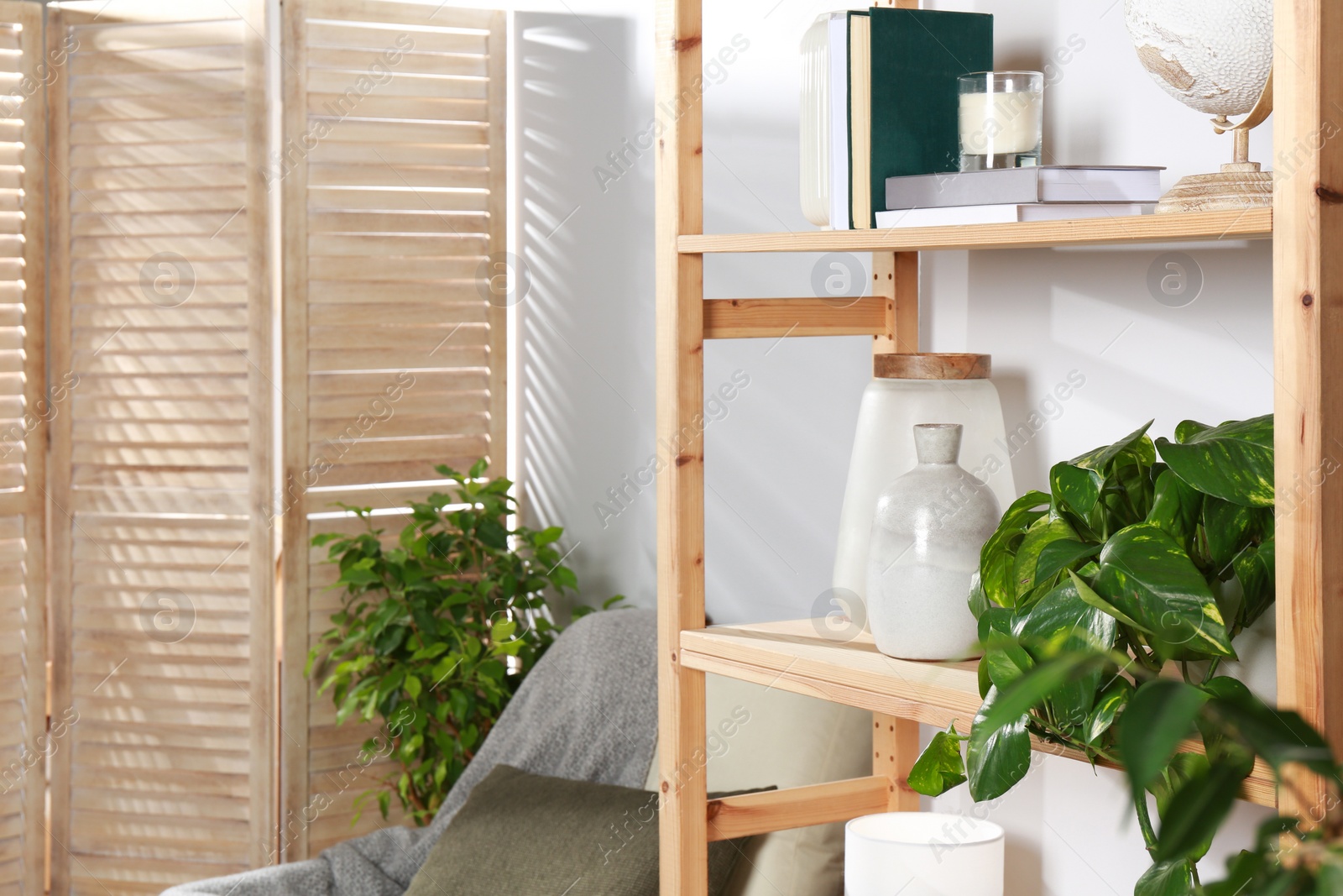 Photo of Wooden shelving unit with home decor, folding screen and armchair near light wall in room. Interior design