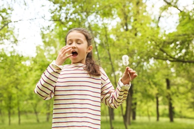 Photo of Little girl with dandelions suffering from seasonal allergy outdoors on sunny day