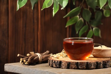 Aromatic licorice tea in cup, powder and dried sticks of licorice root on wooden table, space for text