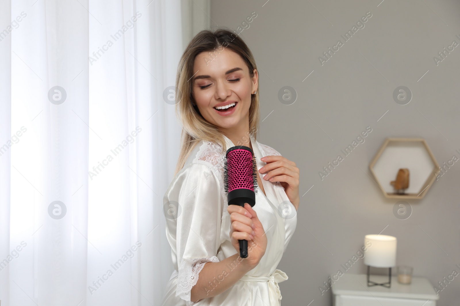 Photo of Beautiful woman with hairbrush singing in bedroom