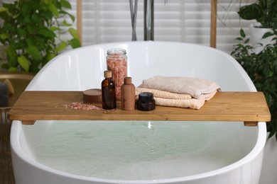 Photo of Wooden board with spa products on bath tub in bathroom