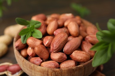 Photo of Fresh unpeeled peanuts and leaves in bowl on table, closeup