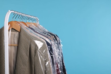 Photo of Dry-cleaning service. Many different clothes in plastic bags hanging on rack against light blue background, space for text