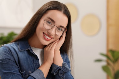 Portrait of beautiful young woman with glasses indoors, space for text. Attractive lady smiling and looking into camera