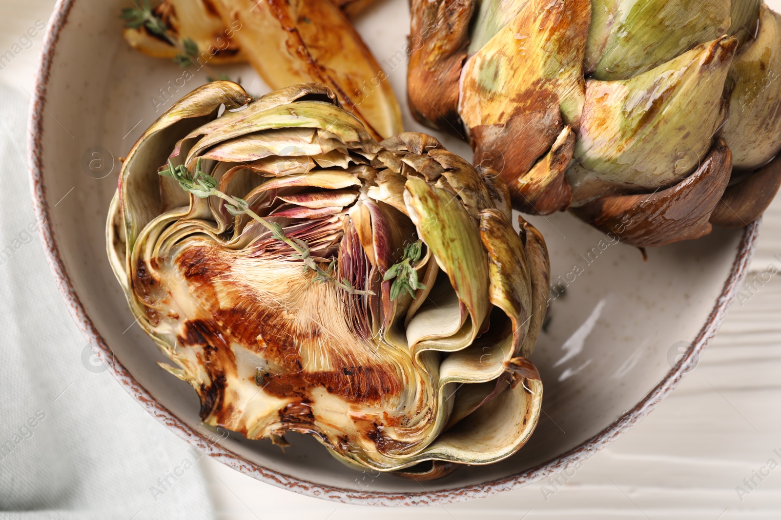 Photo of Bowl with tasty grilled artichokes on table, closeup