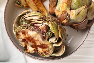 Bowl with tasty grilled artichokes on table, closeup