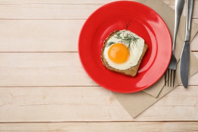 Photo of Plate with tasty fried egg, slice of bread, dill, fork and knife on light wooden table, top view. Space for text
