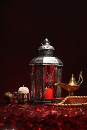 Photo of Arabic lantern, Quran, misbaha, burning candle and Aladdin magic lamp on shiny red table