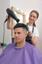 Photo of Professional hairdresser drying client's hair in salon