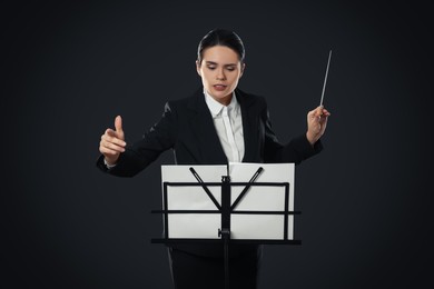 Photo of Professional conductor with baton and note stand on dark background