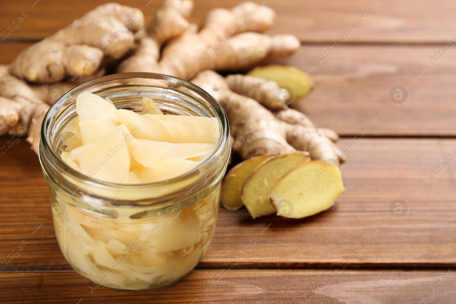 Photo of Spicy pickled ginger and root on wooden table, space for text