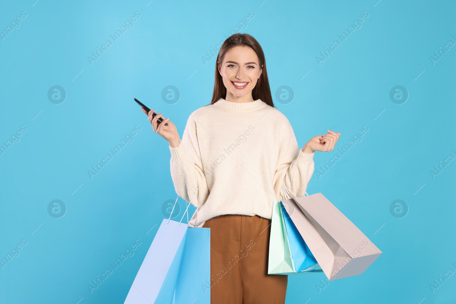 Photo of Happy young woman with shopping bags and smartphone on light blue background. Big sale