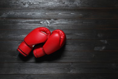 Photo of Pair of red boxing gloves on dark wooden background, flat lay. Space for text