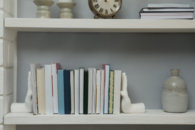 Photo of Hand shaped bookends with books on shelf indoors. Interior design