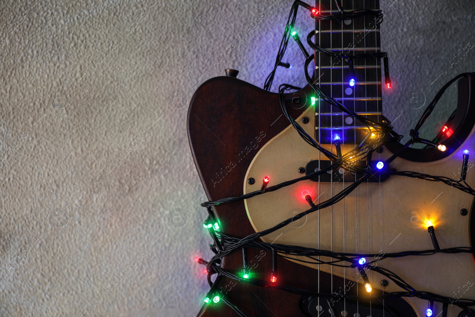 Photo of Guitar with colorful lights on grey stone background, space for text. Christmas music