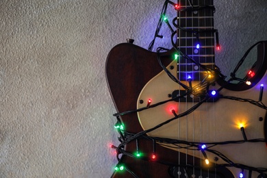 Photo of Guitar with colorful lights on grey stone background, space for text. Christmas music