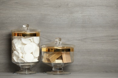 Photo of Composition of glass jar with cotton pads on table near wooden wall. Space for text