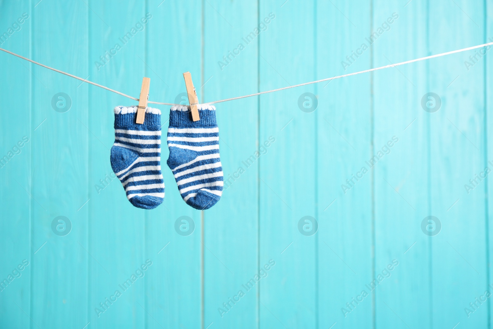 Photo of Baby socks on laundry line against color wooden background, space for text. Child accessories