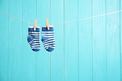 Baby socks on laundry line against color wooden background, space for text. Child accessories