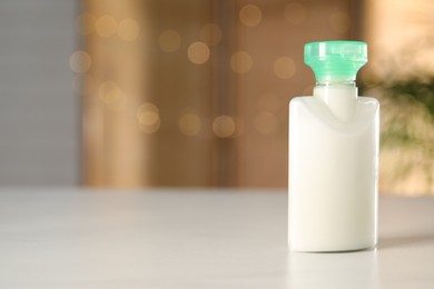 Photo of Mini bottle of cosmetic product on white table against blurred background. Space for text