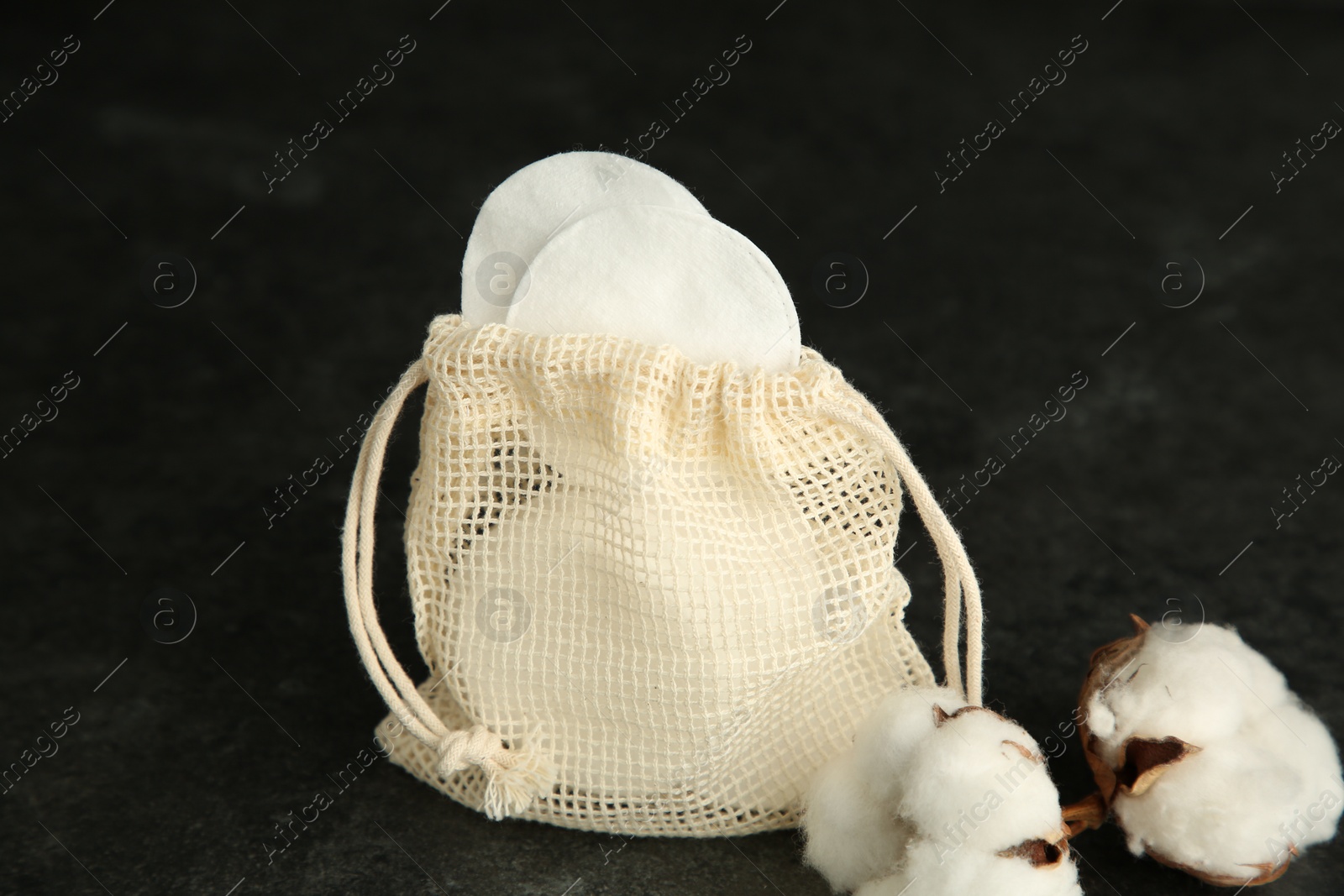 Photo of Cotton pads, bag and flowers on black table, closeup