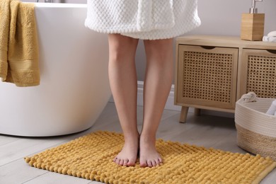 Photo of Woman standing on soft yellow bath mat near tub at home, closeup