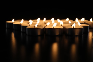 Burning candles on table in darkness, closeup. Funeral symbol