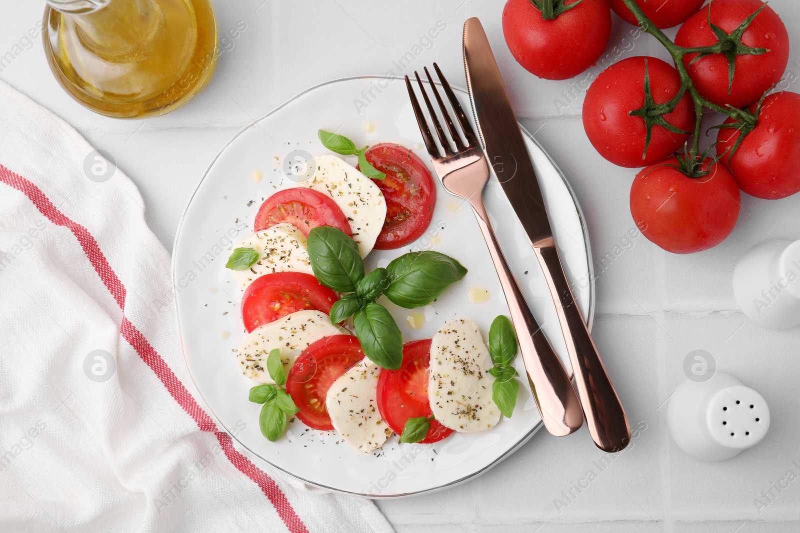 Photo of Caprese salad with tomatoes, mozzarella, basil and spices served on white tiled table, flat lay