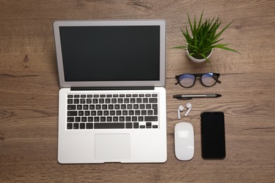 Modern laptop, smartphone and office stationery on wooden table, flat lay. Distance learning