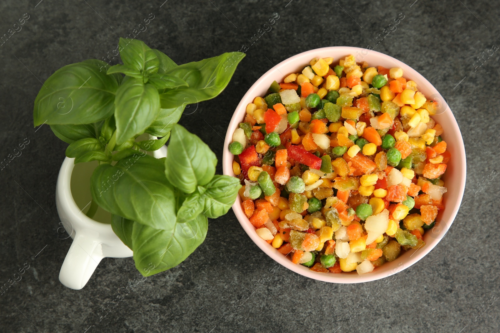 Photo of Mix of different frozen vegetables in bowl and basil on gray table, flat lay