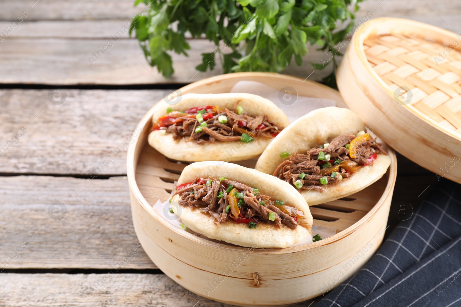 Photo of Delicious gua bao in bamboo steamer on wooden table. Space for text